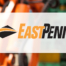 East Penn Logo, orange and black over manufacturing background
